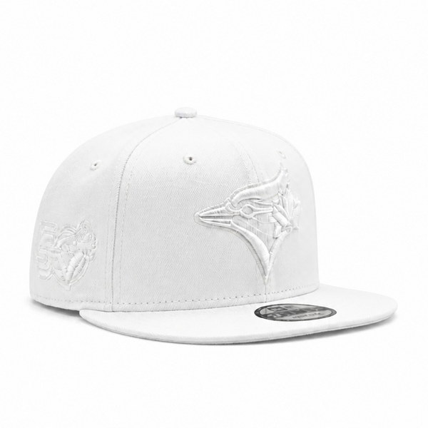 A white flat-brim baseball cap featuring an embroidered white Toronto Blue Jays bird logo on the front and a silver-toned metal visor sticker, set against a plain white background.