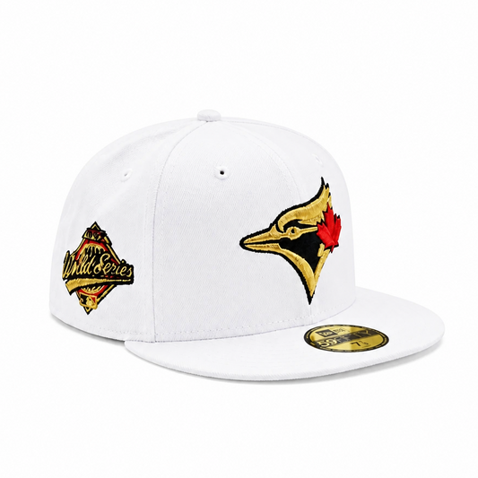 A white structured baseball cap with embroidered Toronto Blue Jays graphics, including a large bird logo on the front and a smaller patch on the side, plus a gold sticker on the brim.