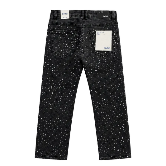 Black denim jeans with a white speckled pattern, shown from the back with a paper tag attached, on a plain white background.