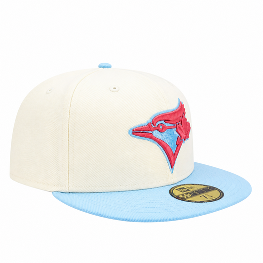 A structured baseball cap with an off-white crown and a light blue flat brim, featuring a red and light blue embroidered Toronto Blue Jays logo on the front and a gold size sticker on the brim.