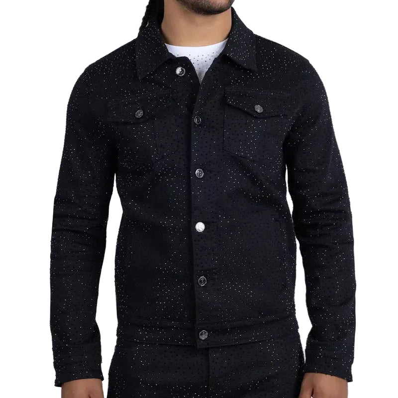 A man wearing a black speckled denim jacket and matching black trousers, standing against a light gray studio background.